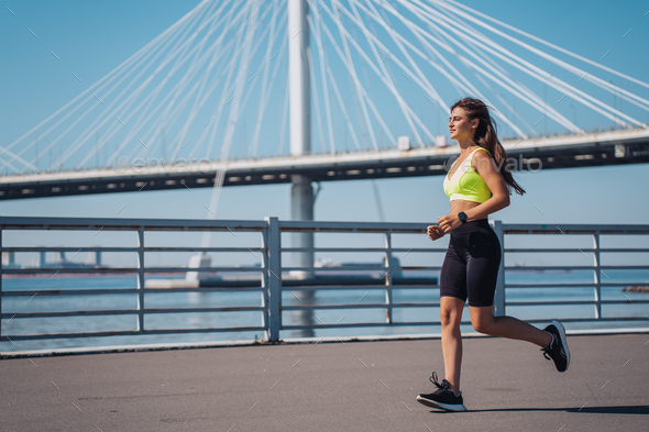 Focused woman jogging in a neon sports bra and black shorts by