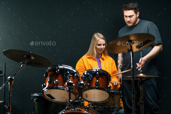 girl in a drum school learns to play a musical instrument with a teacher rehearsing in band's studio