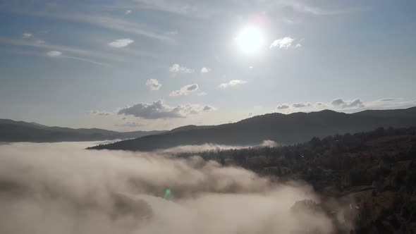 Aerial Drone Flight View Over Low Clouds and Morning Mist Covered Mountain Slopes at Sunrise alt