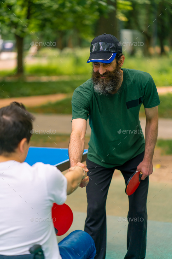 An inclusive disabled man with a racquet in his hand shakes hands with an older man