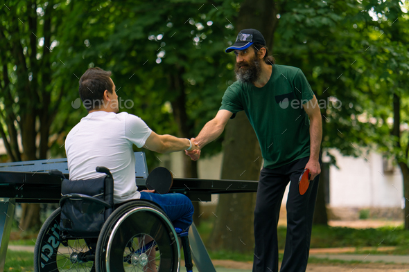 An inclusive disabled man with a racquet in his hand shakes hands with an older man before a game