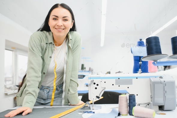 Professional dressmaker woman sews clothes on sewing machine at