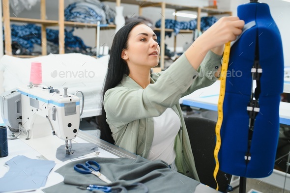 Professional dressmaker woman sews clothes on sewing machine at