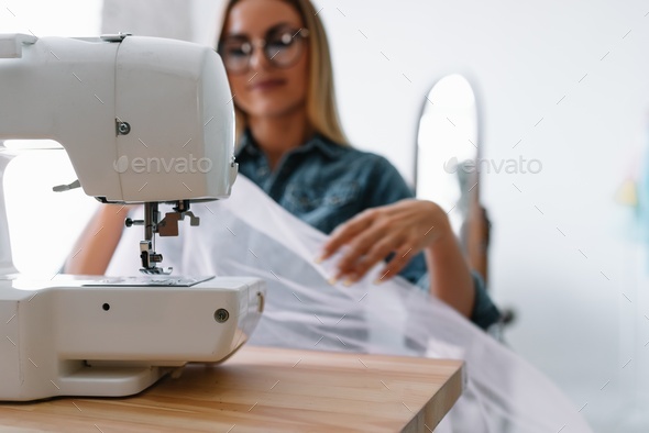 Professional dressmaker woman sews clothes on sewing machine at