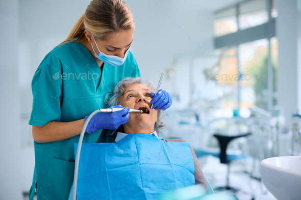 Female dentist performing dental polish procedure on senior patient\'s teeth at dental clinic.