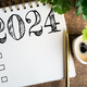 New year resolutions 2024 on desk. 2024 goals list with notebook, coffee cup, plant on wooden table - PhotoDune Item for Sale