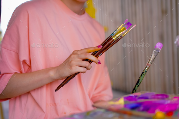 Close-up of girl artist taking paint brushes from a table during an art lesson