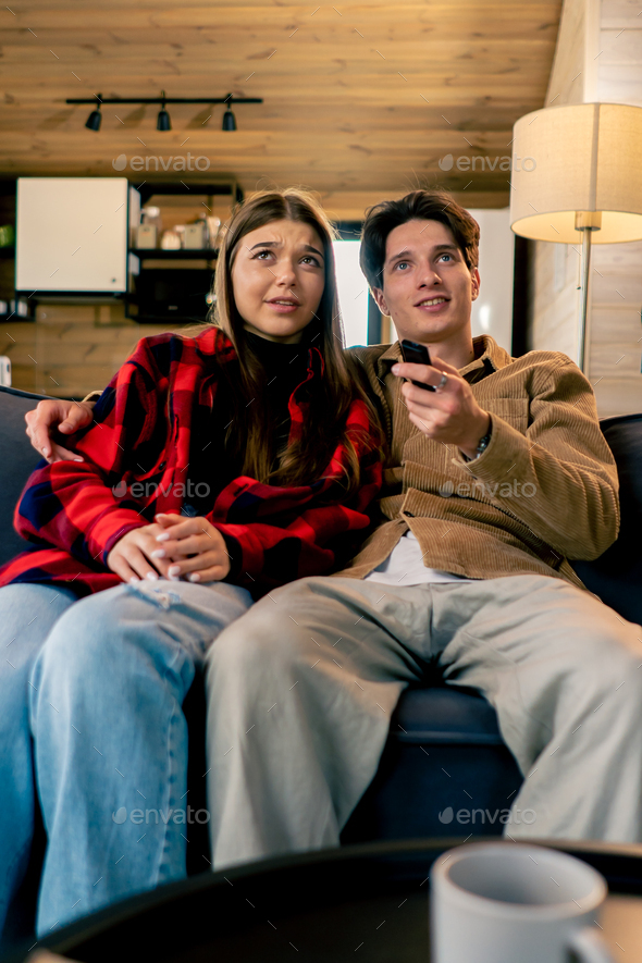 Smiling couple in love a guy and a girl are sitting together on the sofa and watching a comedy film