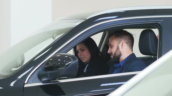 A Man and a Woman Buying a New Car. Buyers Sit in the New Car Showroom