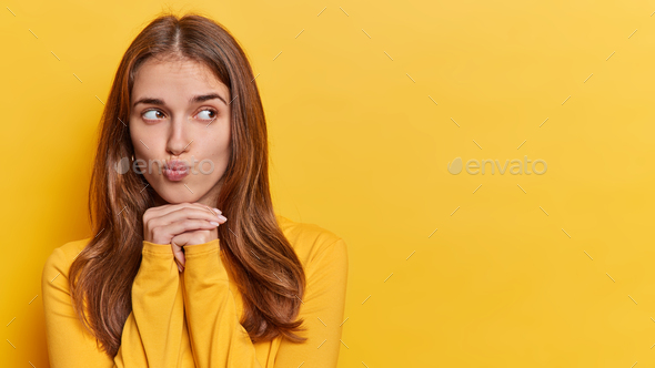 Pensive long haired woman keeps lips folded hands under chin ...