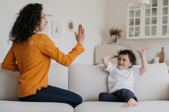 Give me five! Curly young woman teaching son to give five. babysitter playing with kid at kitchen