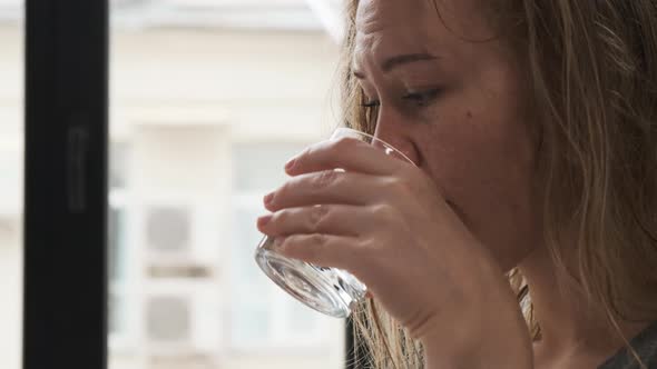 Close Up Beautiful Blonde Sits at Table and Reads Book or Magazine or Looks Into Phone. Drinks Water alt