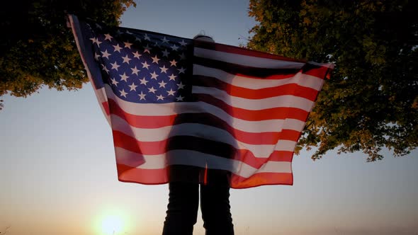 Back View of Happy Woman with USA National Flag Standing Outdoors at Sunset alt