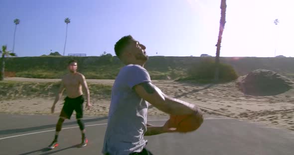 A man does a slam dunk while playing one-on-one basketball hoops on a beach court alt