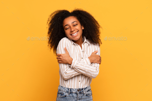 Content woman hugging herself with joyful smile, yellow background