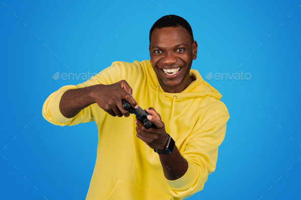 A joyful Black man in a yellow hoodie wields a game controller with dynamic enthusiasm