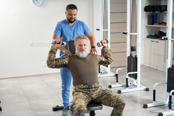 Man in camouflage clothes works out in gym in rehabilitation center