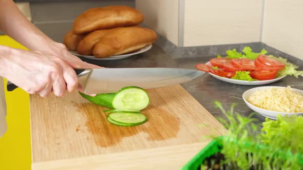 Women's hands cut cucumber for making sandwiches on a wooden cutting board.