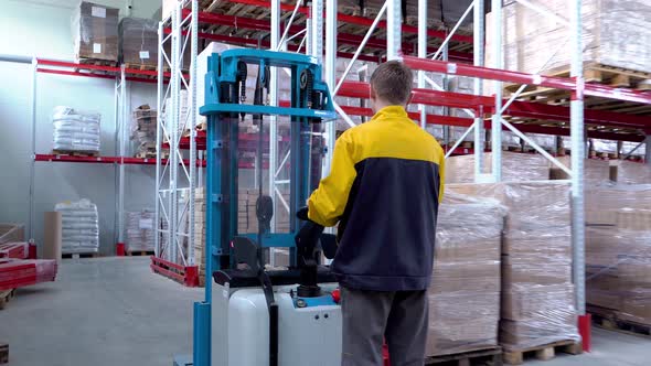 Warehouse Worker Driver in Uniform Loading Cardboard Boxes By Forklift Stacker Loader alt