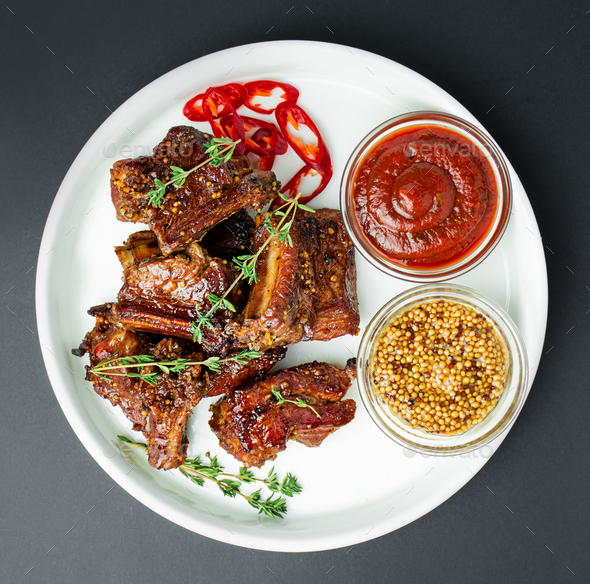 Baked ribs on a white plate. Roasted pork ribs with spices and herbs on a dark background.