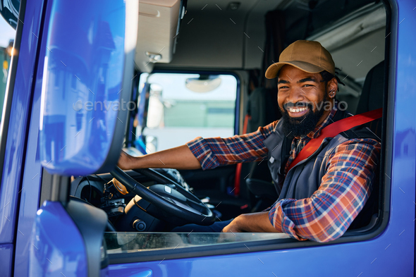 Happy black truck driver behind steering wheel in a cabin looking at camera.