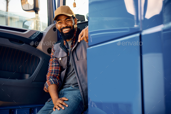 Happy black truck driver sitting in vehicle cabin and looking at camera.