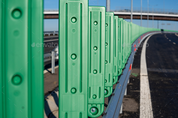 Green metallic fence posts lining the side of an asphalt road