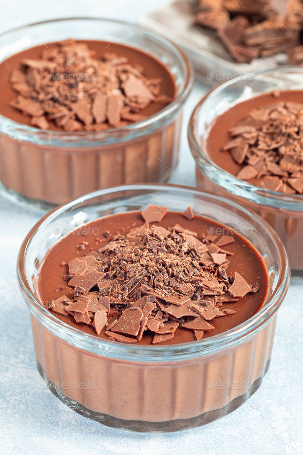 Chocolate Panna Cotta dessert in glass ramekin, wooden board and chocolate on background