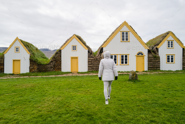 Woman walking towards Facades of the Glaumbaer Three turf houses in Iceland - Stock Photo - Images
