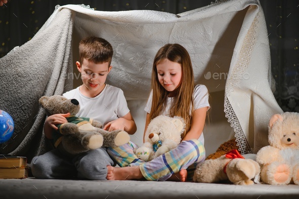 Two little children play at home in the evening to build a camping tent to read books