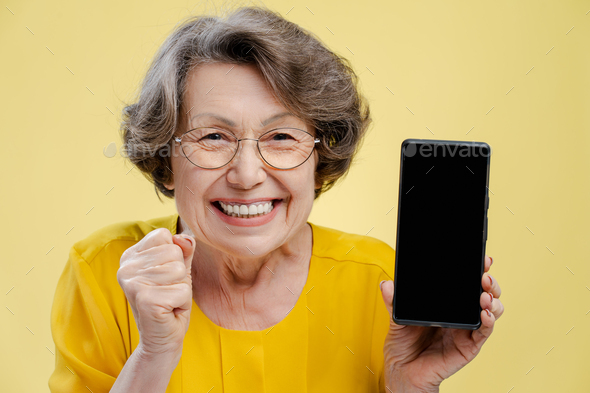 Portrait of smiling grandmother wearing eyeglasses holding mobile phone ...