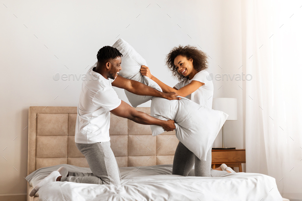 Black Couple Having Pillow Fight Laughing And Flirting In Bedroom