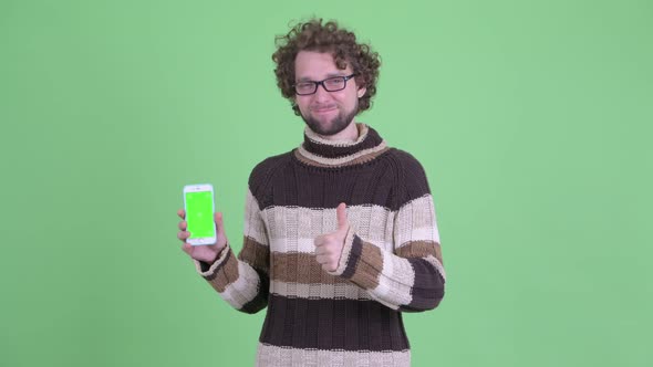 Happy Young Bearded Man Showing Phone and Giving Thumbs Up alt