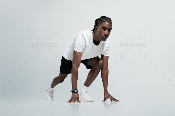 Focused black man in athletic wear poised in starting position for sprint  Stock Photo by Prostock-studio