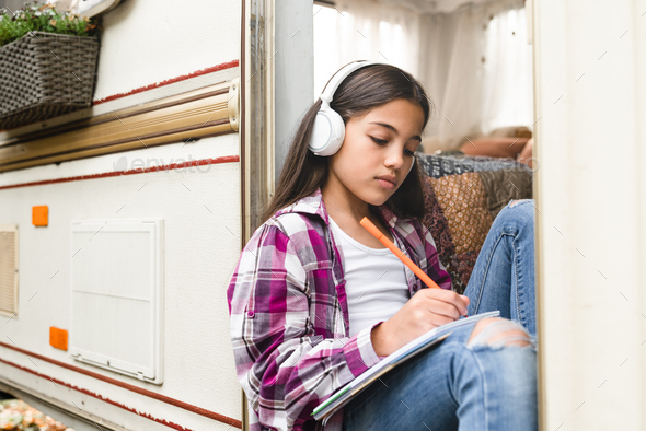 Small preteen learner girl kid child listening to the music drawing doing homework while traveling