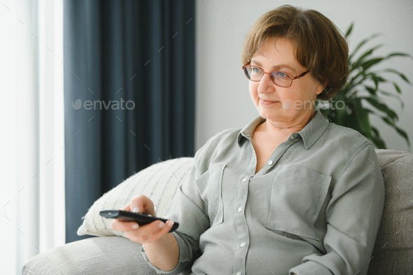 Elderly woman making hearing sign, rising tv set volume with remote control.