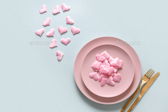 Valentine\'s day table setting with pink romantic hearts and golden cutlery on blue background.