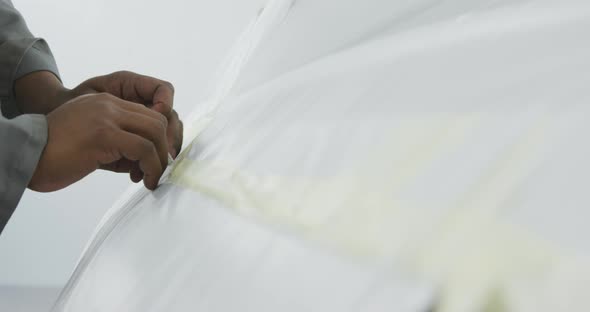 African American male car mechanic cutting a protective cover on a car with a razor blade alt