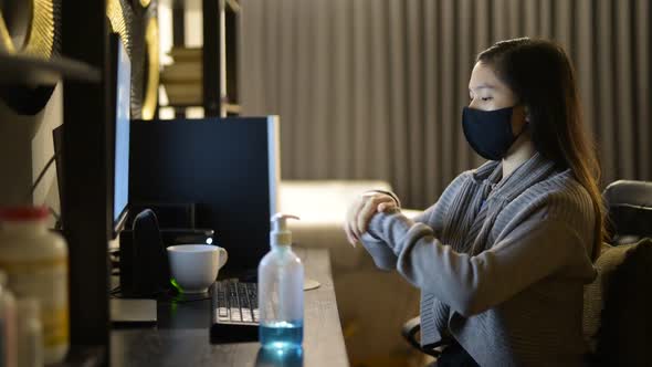 Young Asian Woman with Mask Using Hand Sanitizer While Working From Home at Night alt