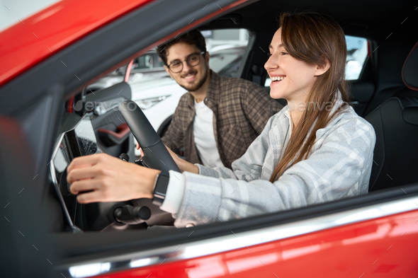 Man and woman sitting on new car choosing new vehicle in auto showroom