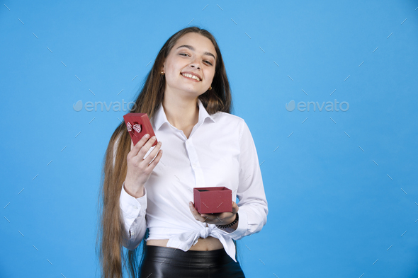 Cheerful adorable woman in blouse, unpacking lovely tiny gift box, while  looking at camera.