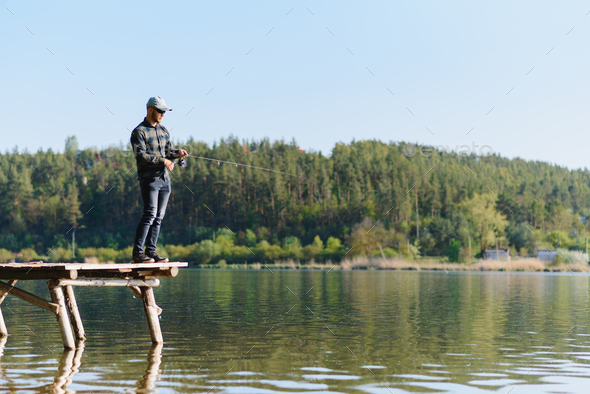 Fisherman With Rod Spinning Reel On The River Bank Fishing For