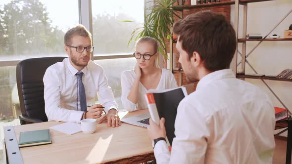Caucasian Male Boss with Glasses and Light Bristle Sitting at Table with Female Secretary Discussing alt