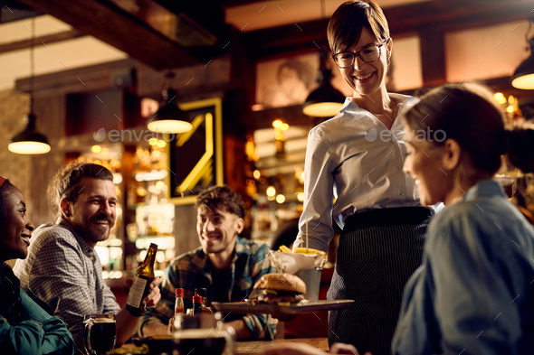 Happy waitress serving food to guests in a pub.