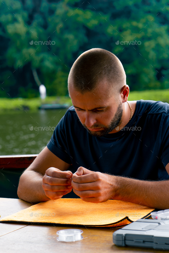 a young man strings a fishing line or a fly on hook for fishing feeder free  style method Stock Photo by guyswhoshoot