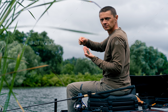 Portrait of a serious fisherman stringing a bait on the hook of fishing rod  for catching river fish Stock Photo by guyswhoshoot