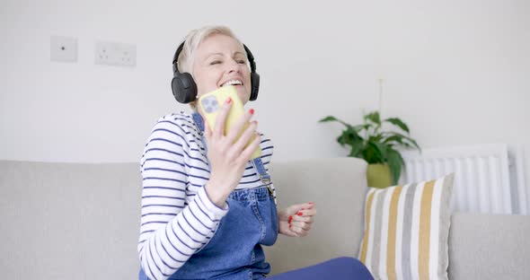 Mature woman sitting on couch enjoying music with headphones