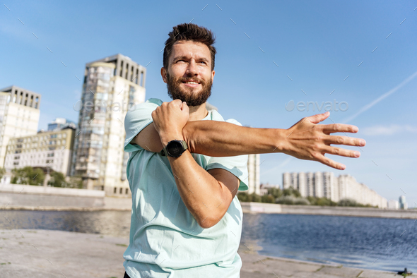 Active man performing a stretch routine along a river promenade with ...