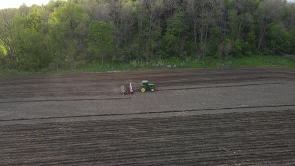 aerial view of farmer fertiziling and seeding last portion of farm field. Hill covered with woods.