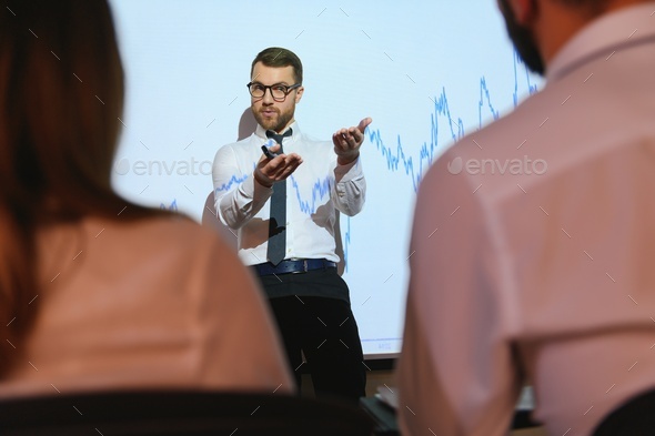 Trading teaching. Male leader talking to employees, showing the plan on the projector in office